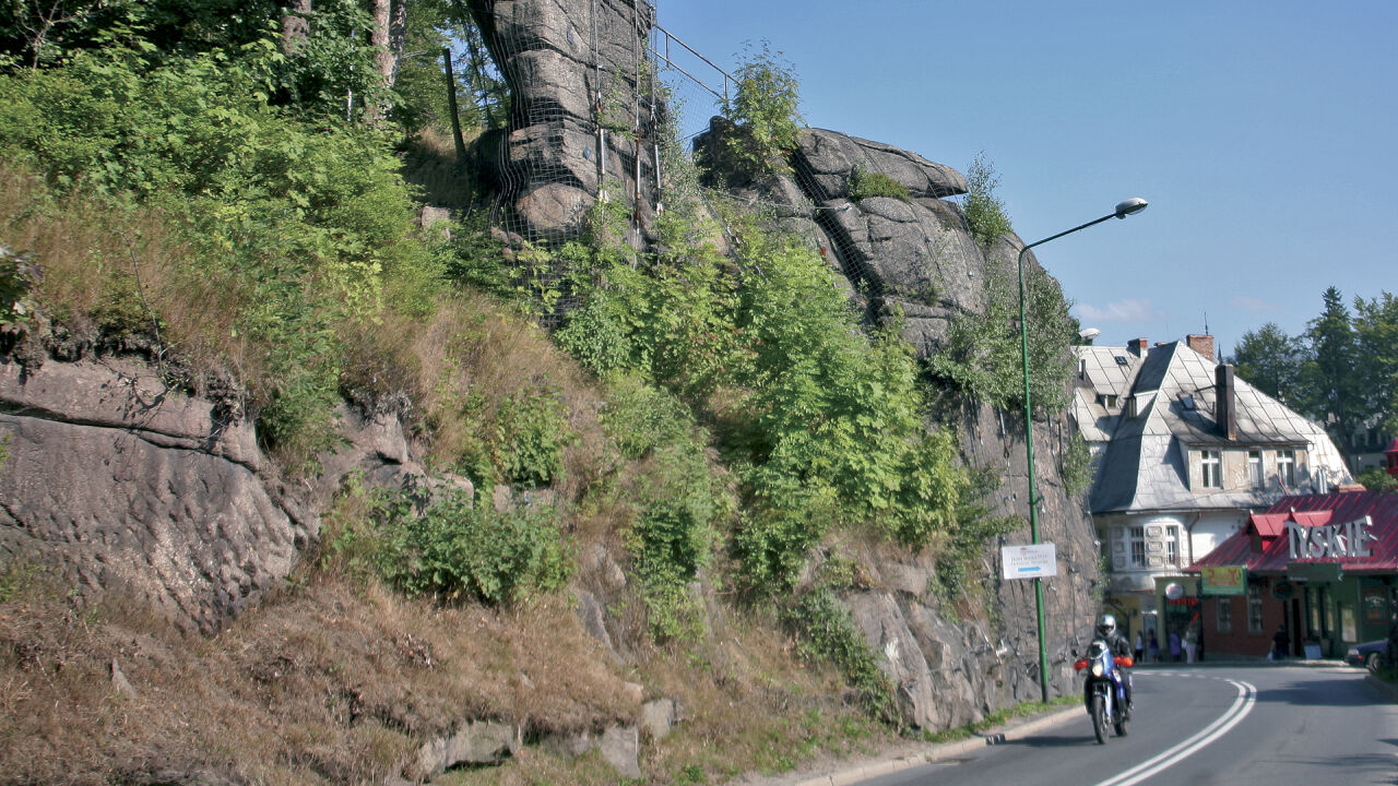 Motorrad auf einer Ortsstraße unter einer Felswand, daneben ein Haus mit Leuchtreklame Motorrad auf einer Ortsstraße unter einer Felswand, daneben ein Haus mit Leuchtreklame